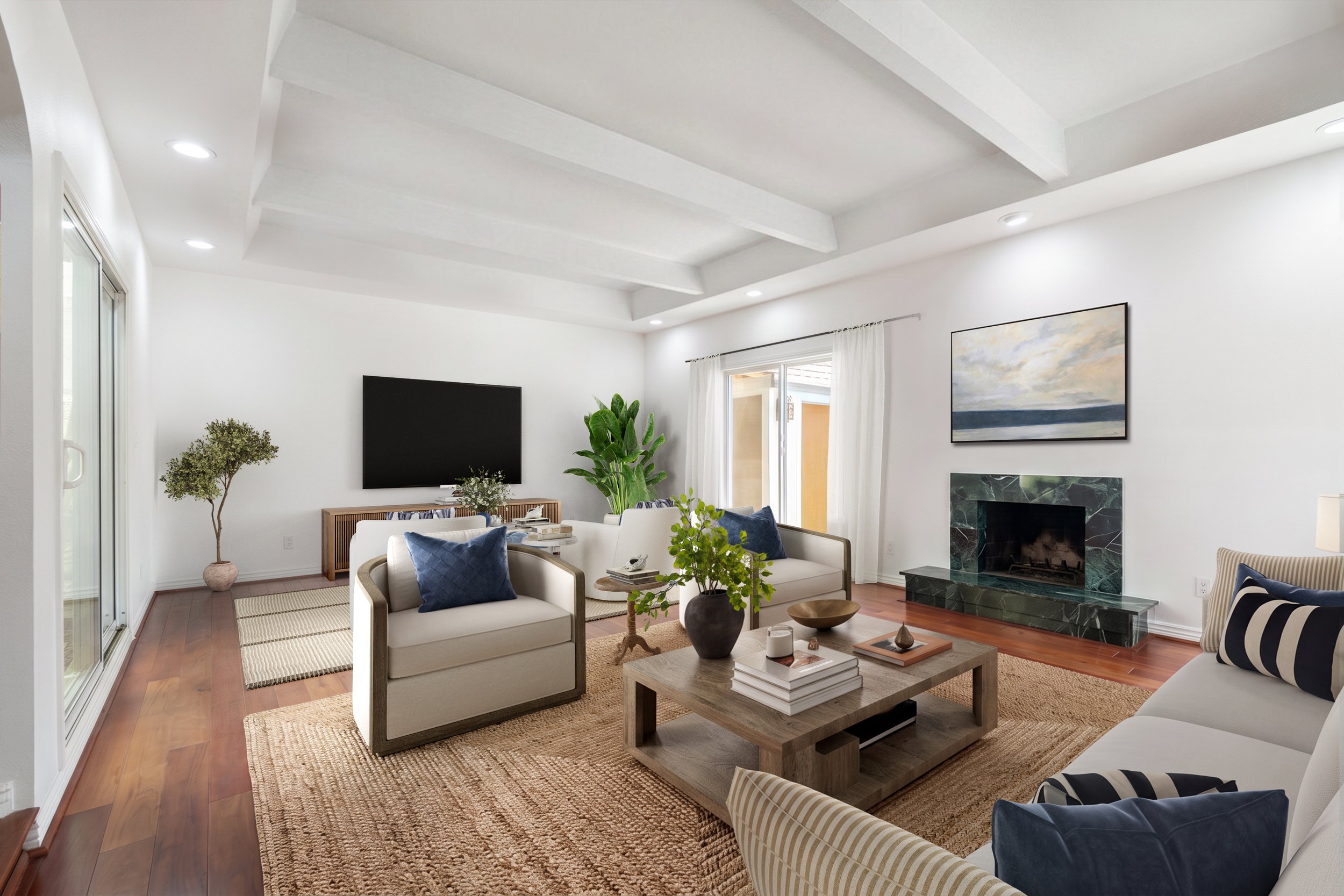 Living room with white walls, wooden flooring, a green marble fireplace, large windows with white curtains, a flat-screen TV, and various seating including cream-colored armchairs with blue and beige cushions, decorated with plants and artwork.