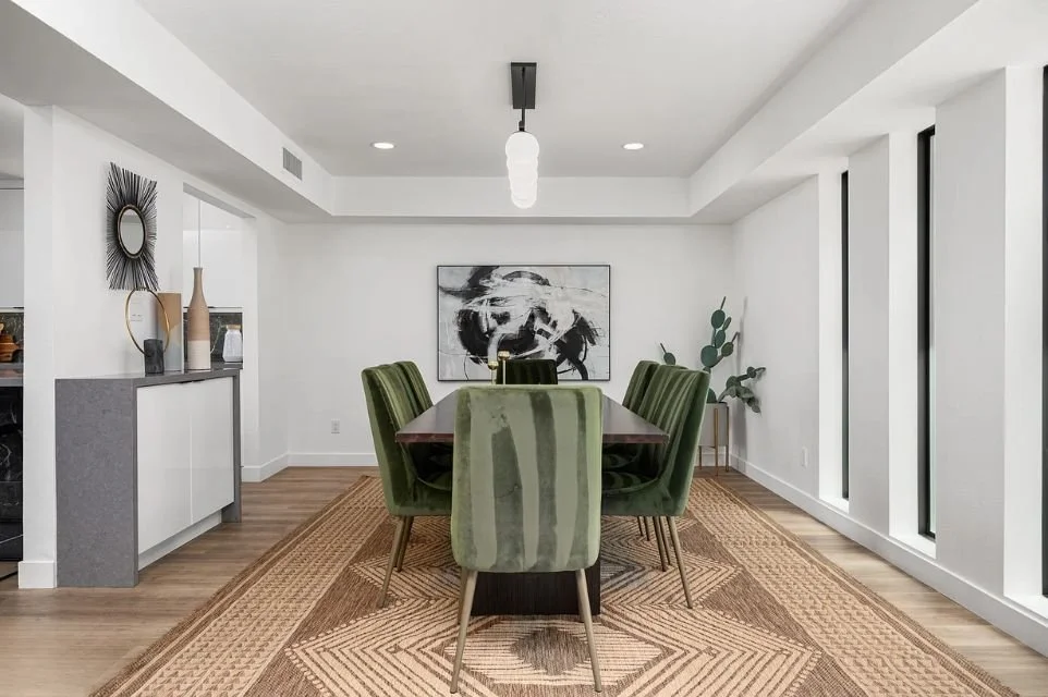 Modern Phoenix dining room with upholstered green chairs, wood table, textured area rug, minimalist decor, and natural light from vertical windows in an open-concept layout