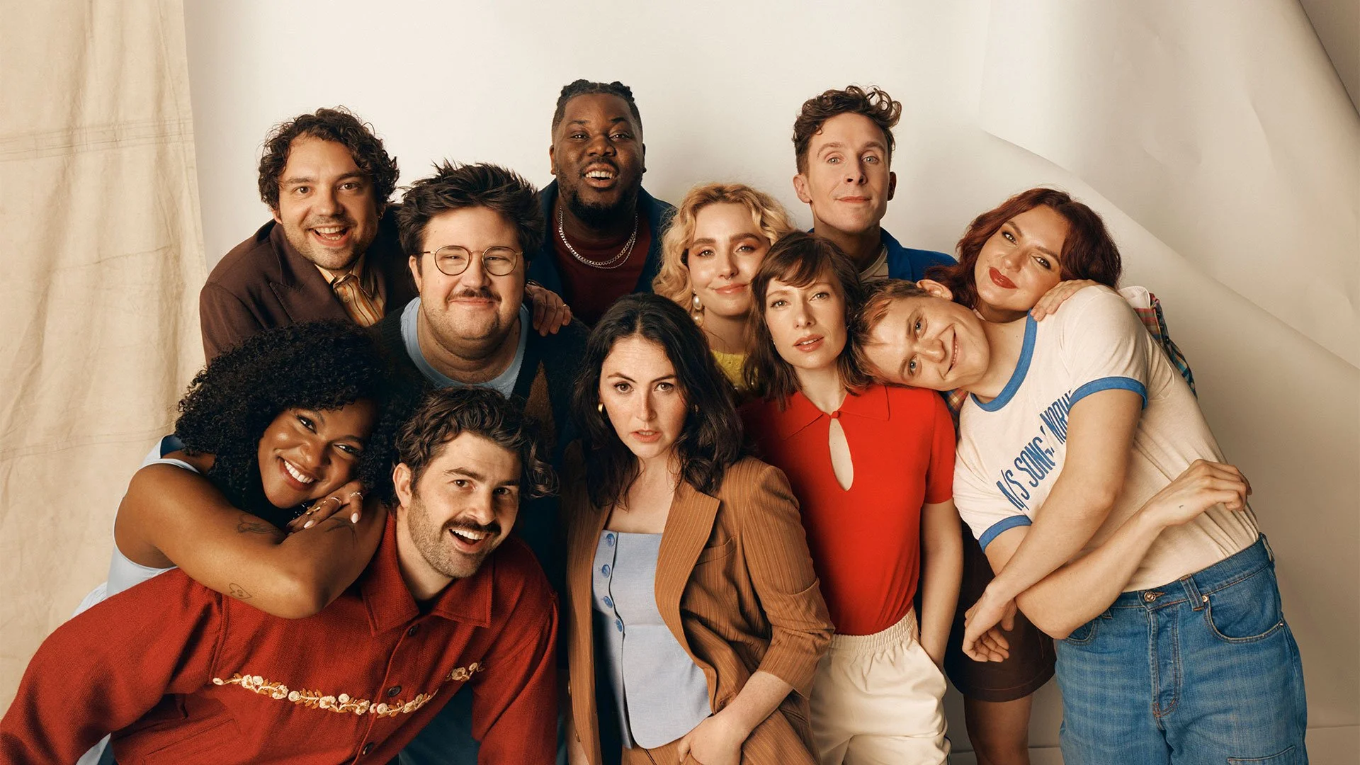 Group of diverse young adults smiling and hugging, posing together against a neutral background.