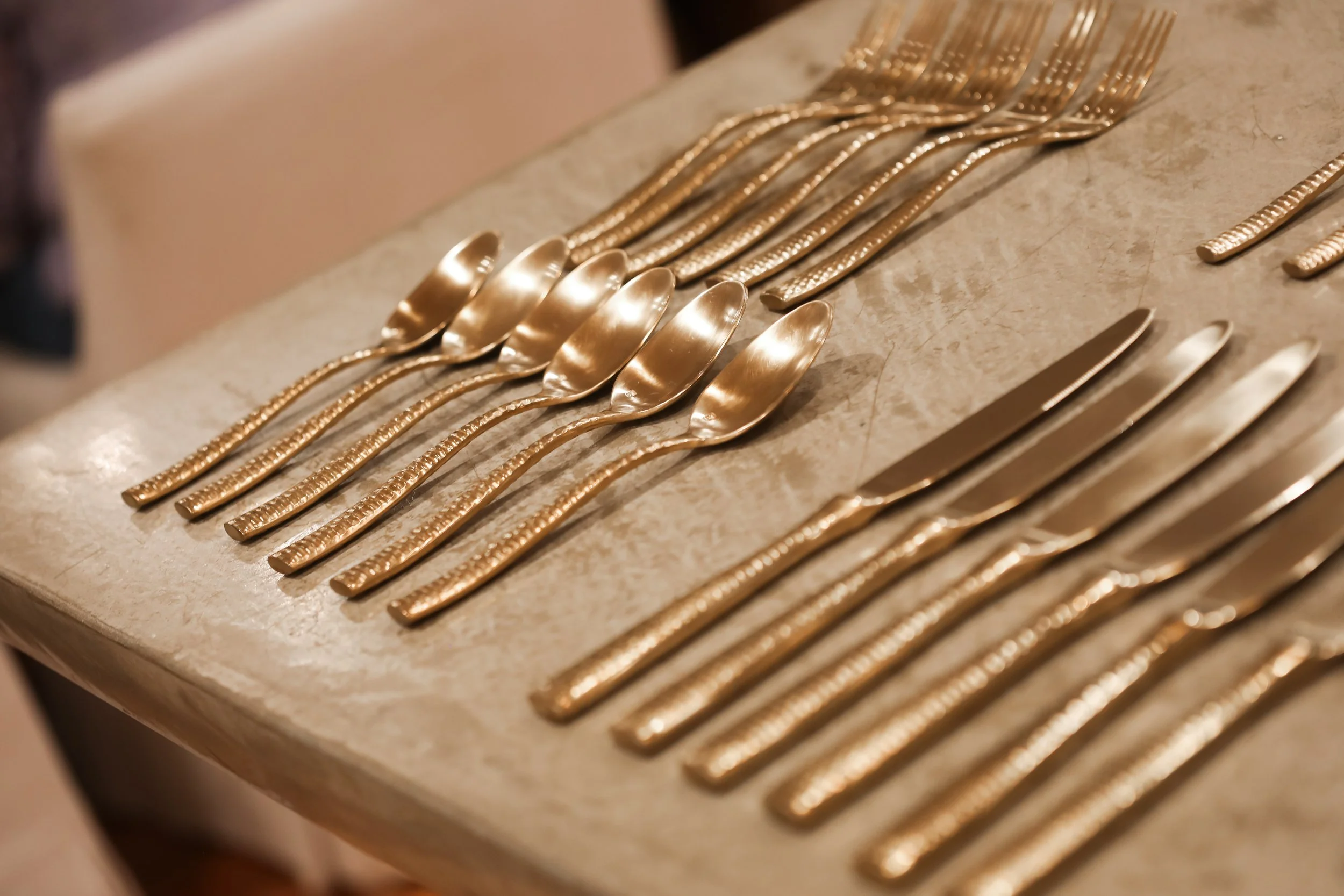 Multiple gold-colored forks, knives, and spoons arranged on a marble surface.