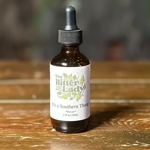 A small brown glass bottle with a dropper cap and a white label that reads "The Bitter Lady," featuring green leaves and a flavor description of "It's a Southern Thang."