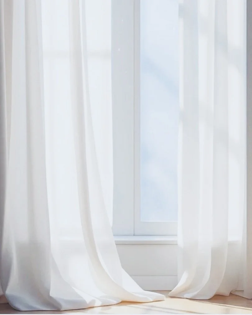 White curtains slightly parted in front of a glass door leading outside, with sunlight streaming through.