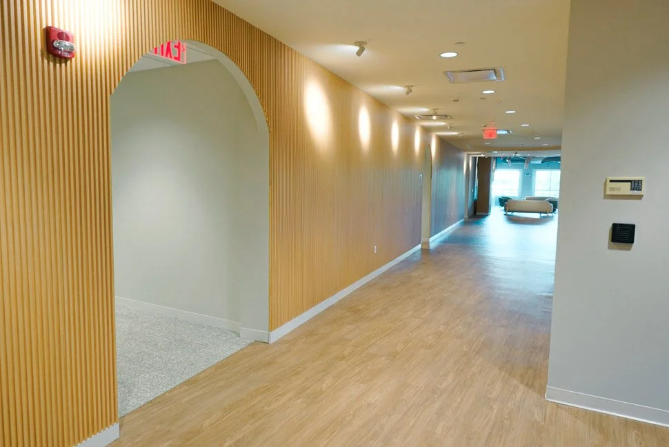 Empty hallway in a modern building with wooden wall paneling, a seating area at the end, and an illuminated exit sign.
