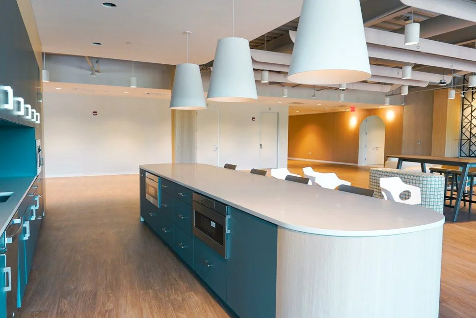 Modern kitchen with blue cabinetry, large white island, chef appliances, hanging pendant lights, and adjacent open seating area with tables and chairs.