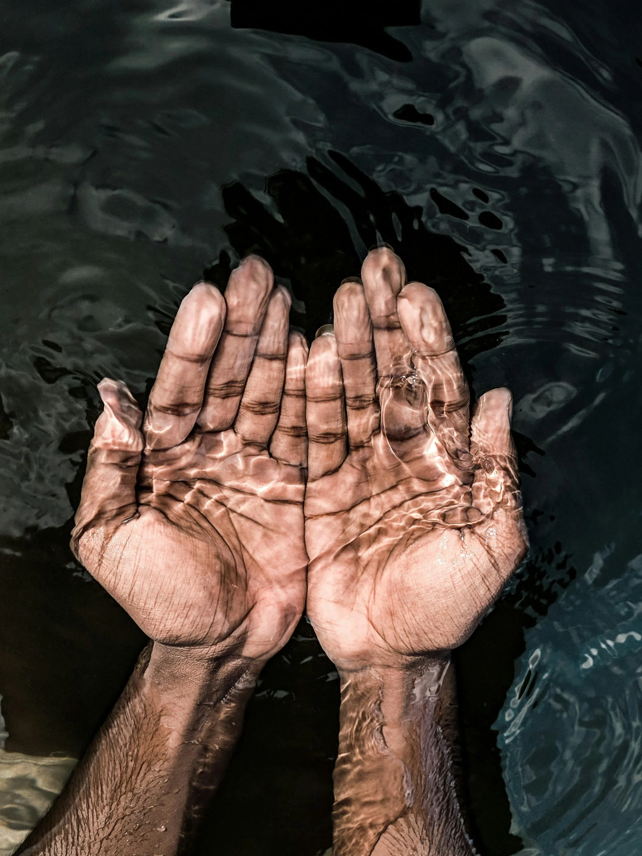 Two hands held with palms together submerged in dark water.