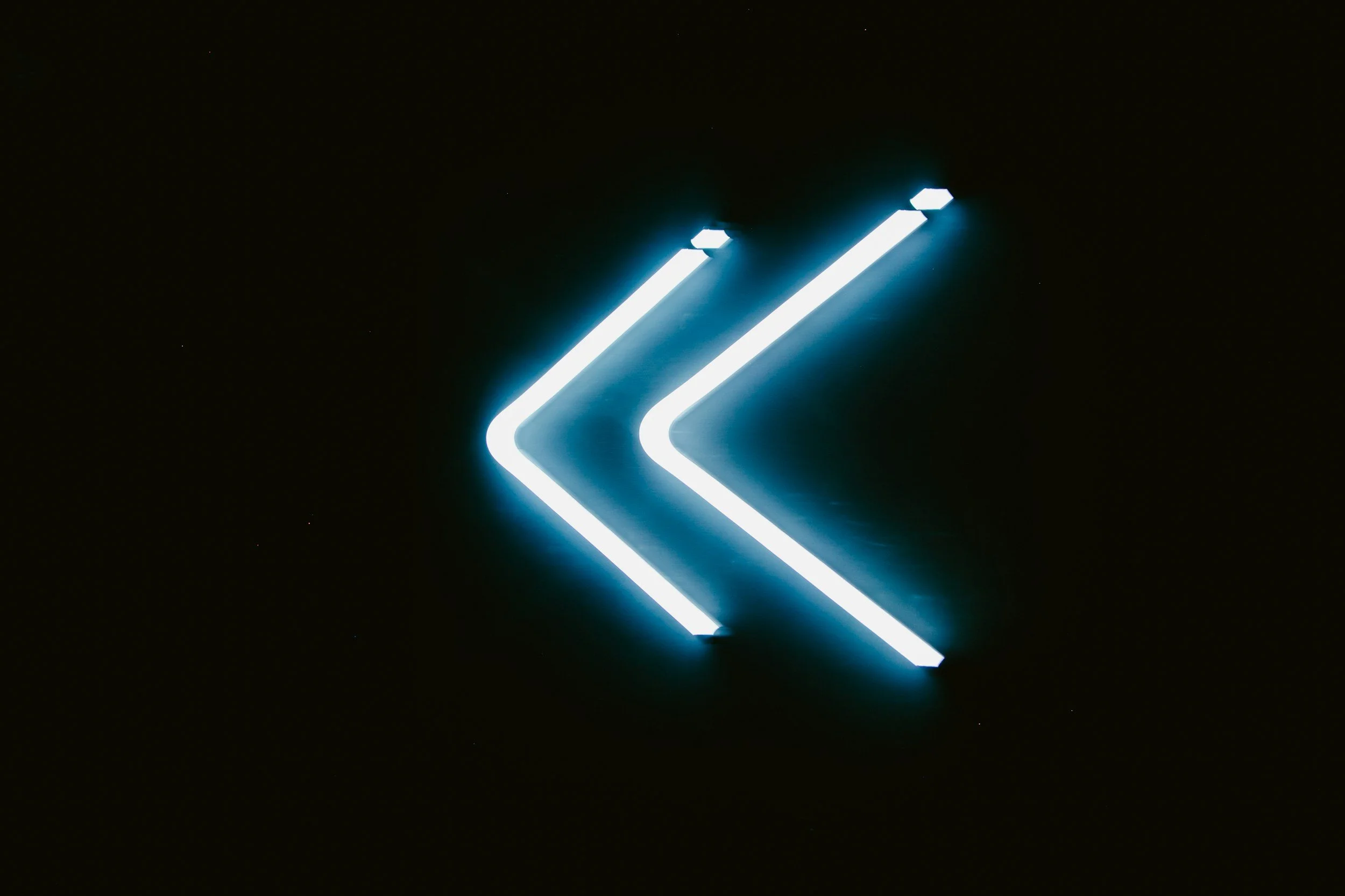 Neon sign with two blue arrows pointing to the left.