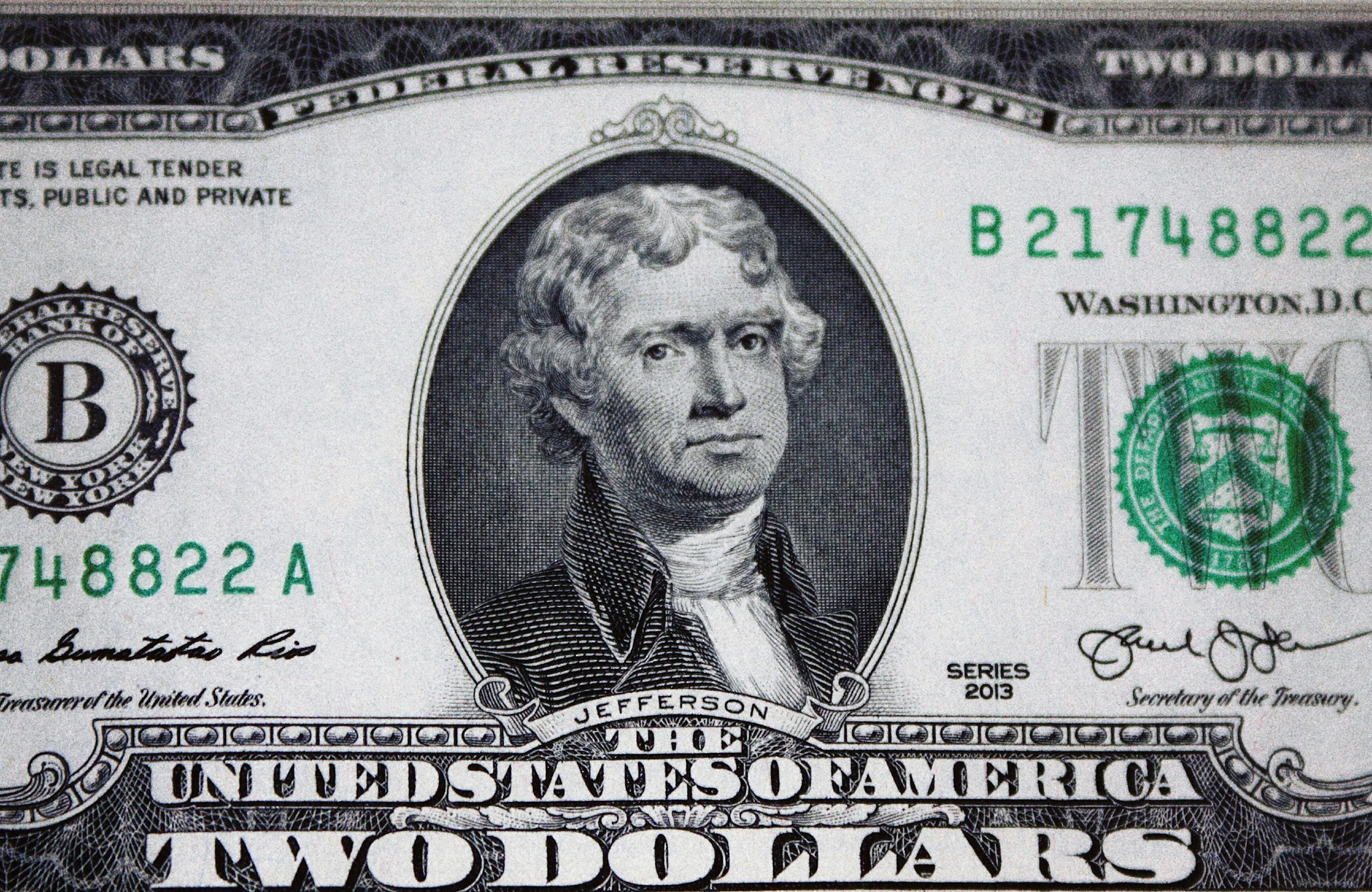 Close-up of a United States two-dollar bill featuring a portrait of Thomas Jefferson in the center, with green serial numbers and black text, and decorative border details.