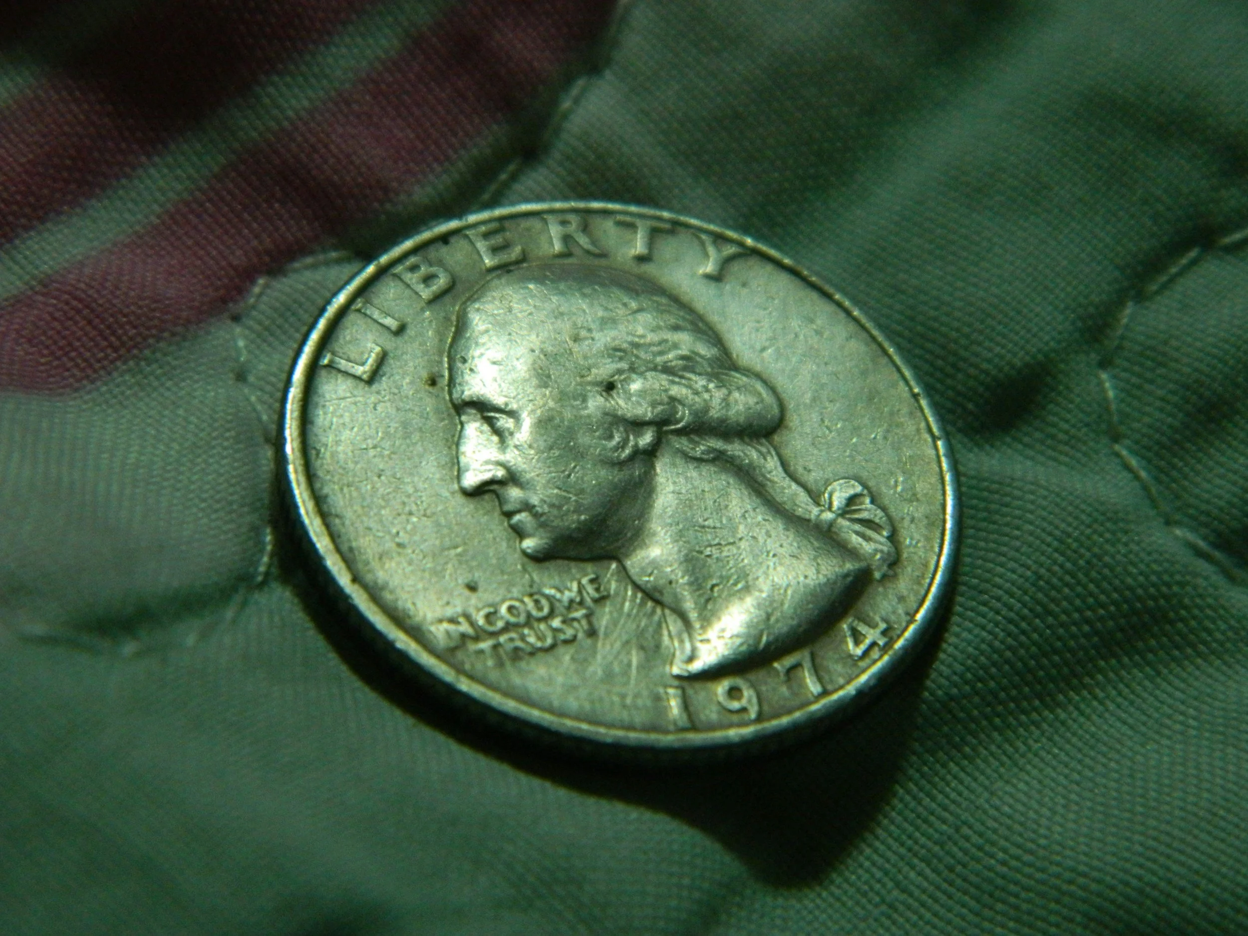 A 1974 U.S. quarter coin showing a profile of George Washington's head against a green fabric background.