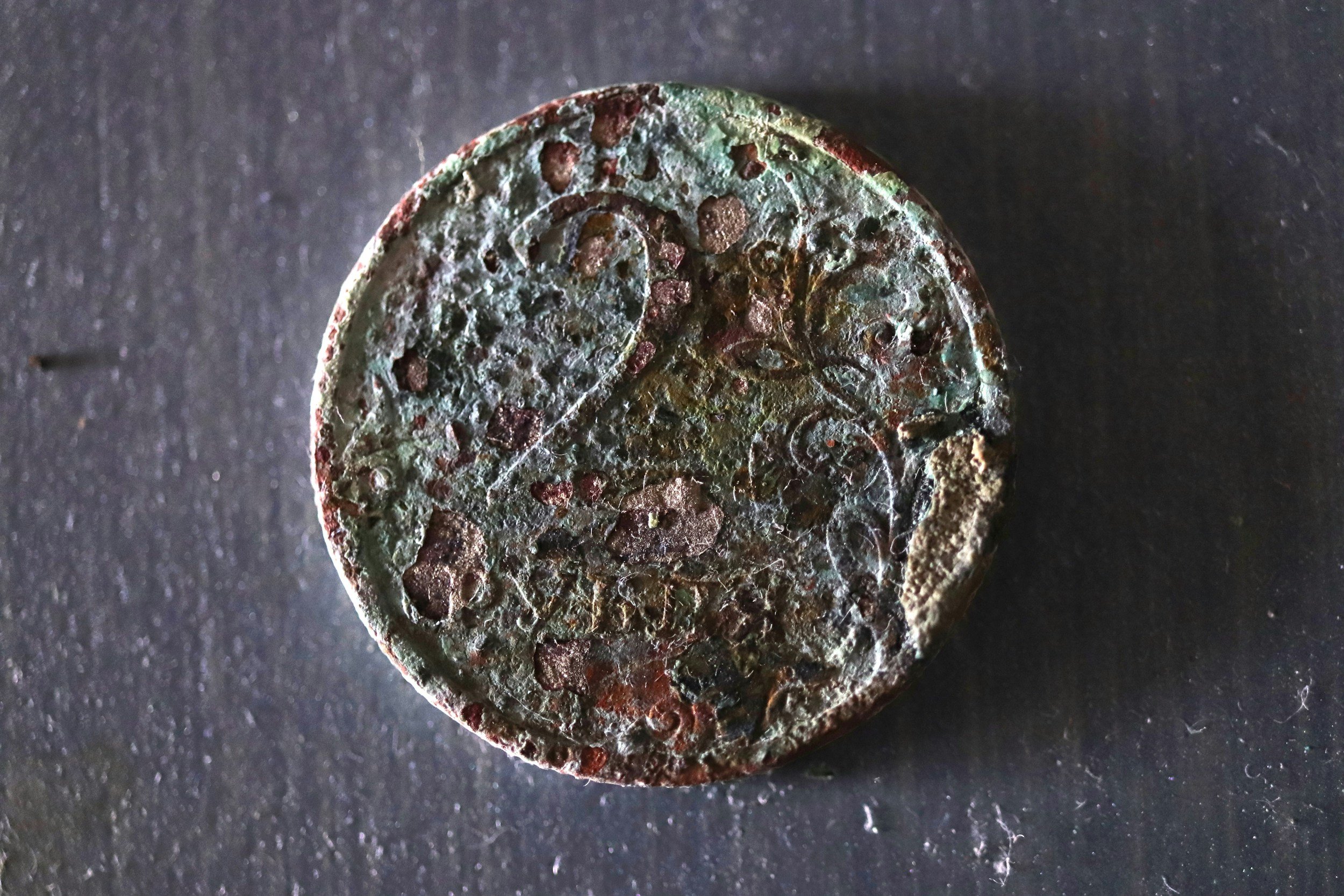 Close-up of an old, corroded coin resting on a dark surface.