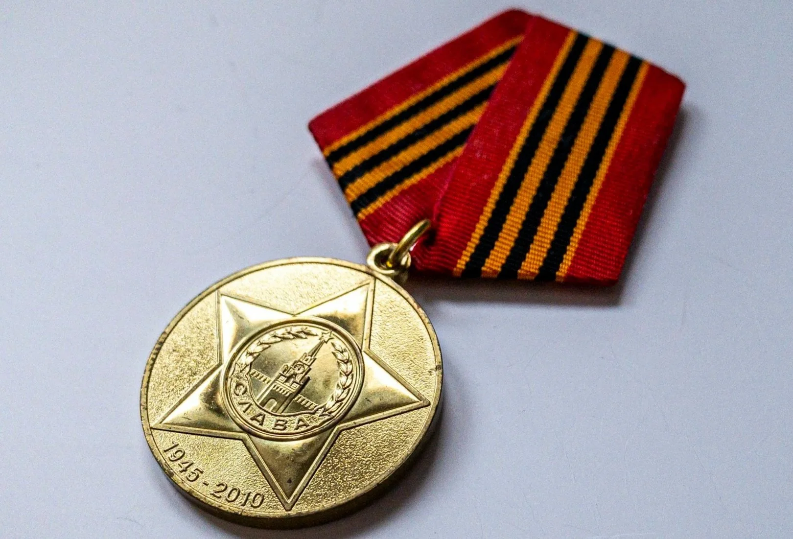 A medal with a gold-colored circular shape, featuring a star and a crest with a tower, hanging from a red and black striped ribbon.