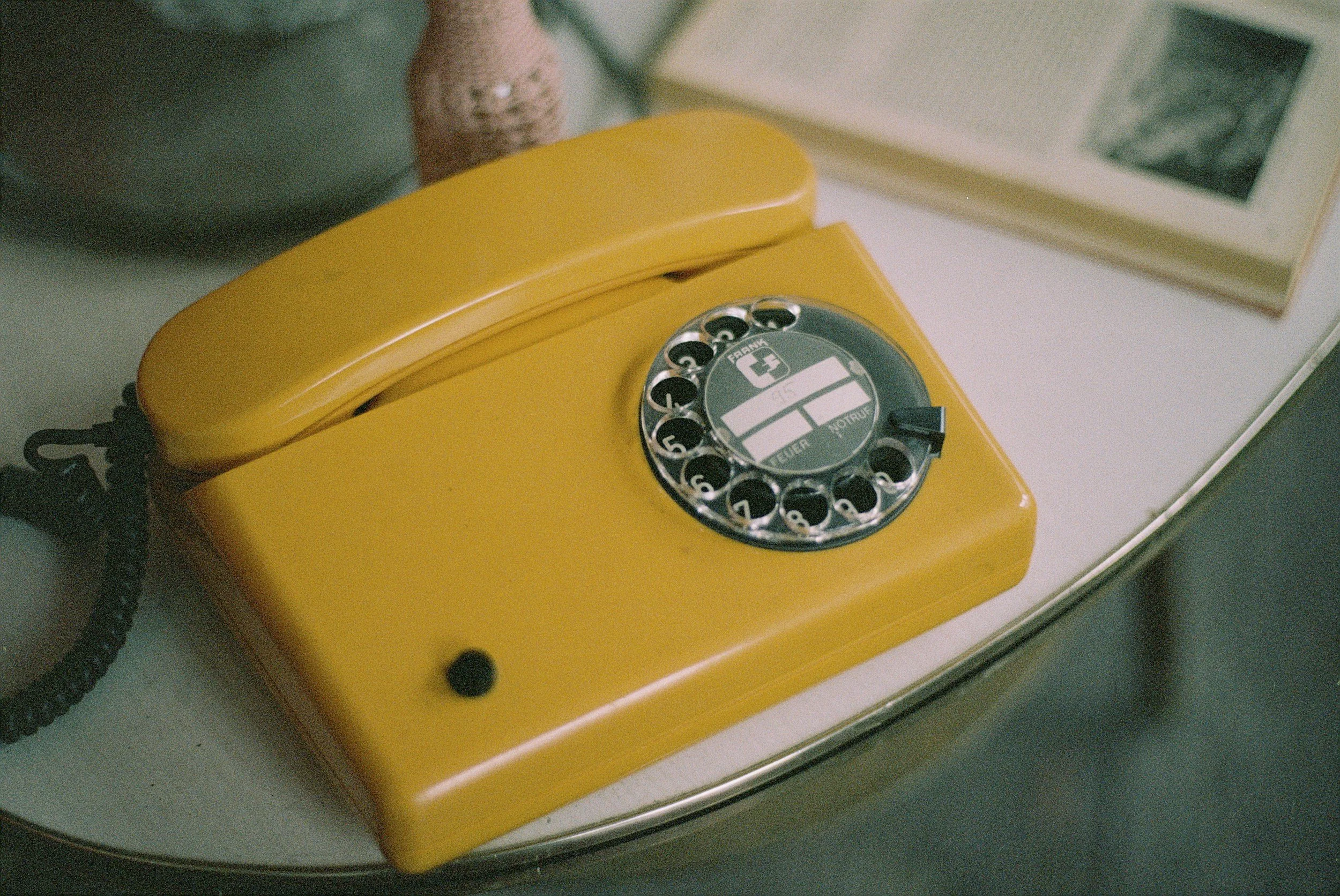 A yellow rotary dial telephone placed on a metallic surface, with a black cord attached.
