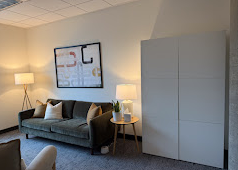 Living room with a dark gray sofa, white side tables with lamps, a large white wardrobe, and a wall art print.