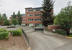 A multi-story brick building with large windows, surrounded by trees and greenery, with a concrete ramp leading up to it.