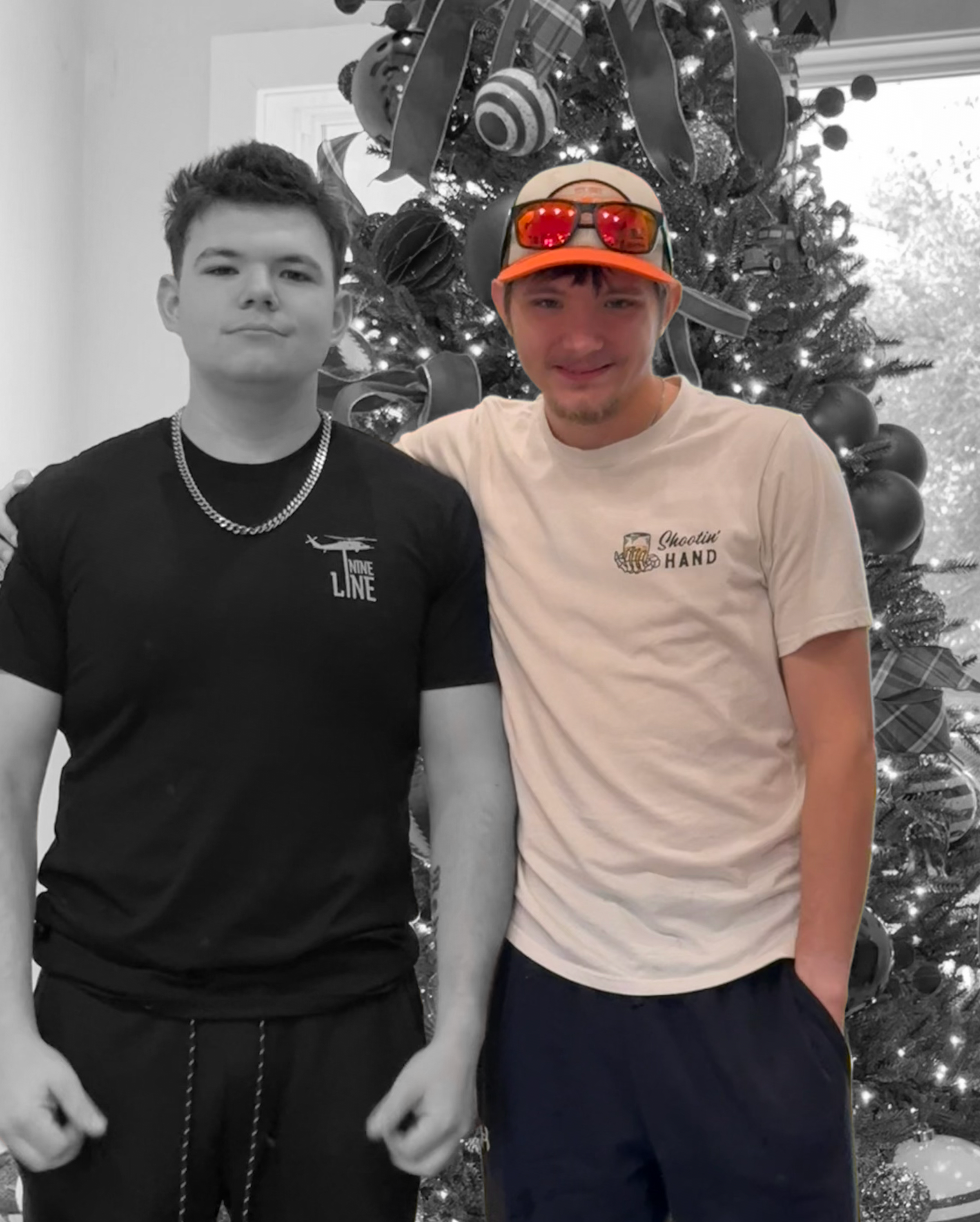 Two boys stand in front of a decorated Christmas tree. The image is in color with one boy wearing a black shirt with a chain necklace, and the other boy wearing a white t-shirt, cap, and sunglasses. The second boy is smiling, and the first boy has a neutral expression.