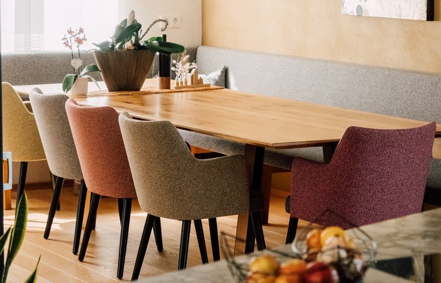 Ein Holztisch mit bunten Polsterstühlen in einem modernen Raum, dekoriert mit Blumen und kleinen Gegenständen.