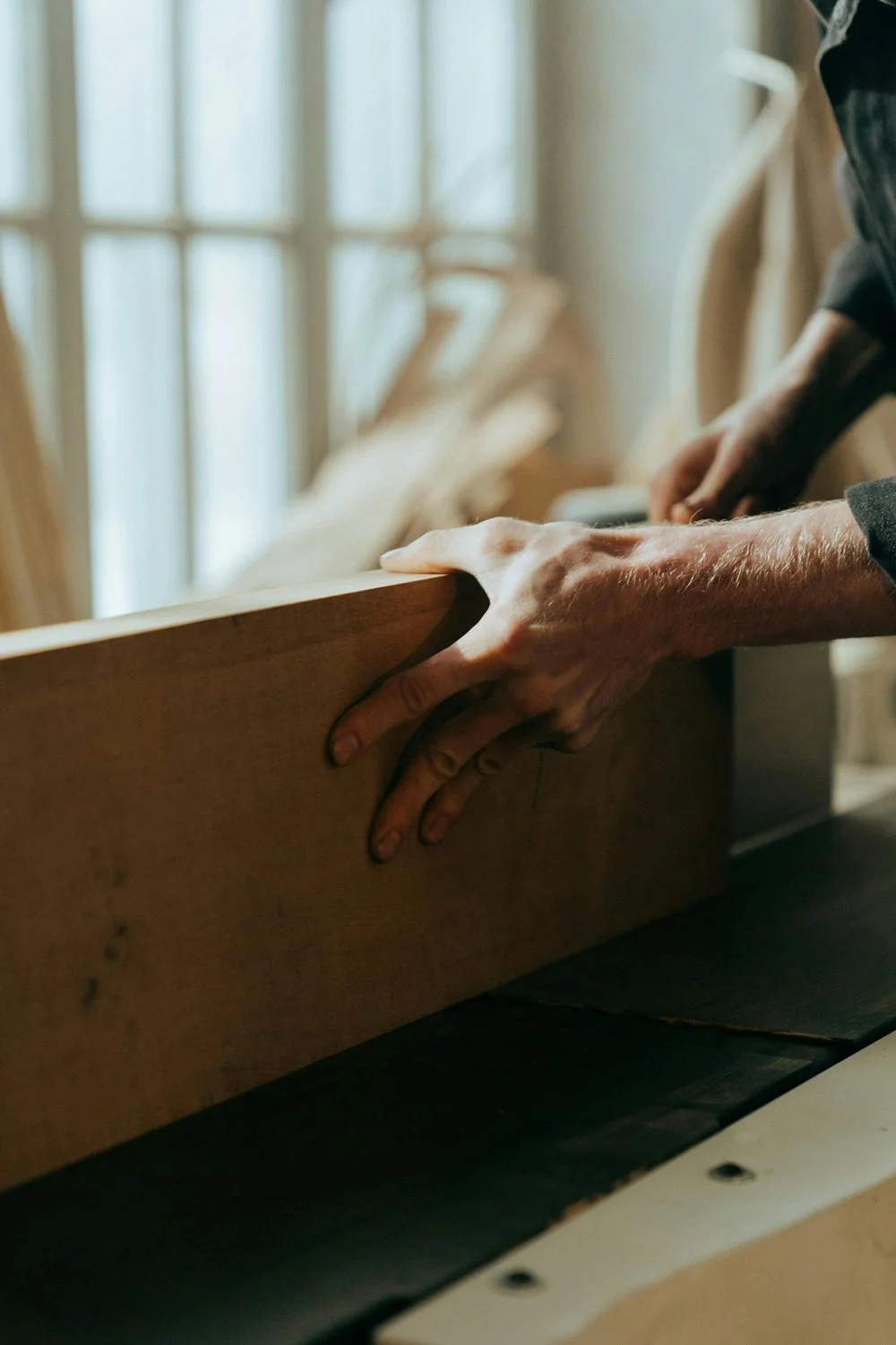 Nahaufnahme der Hände eines Handwerkers, der Holz bearbeitet, bei Sonnenlicht in einem Holzatelier.