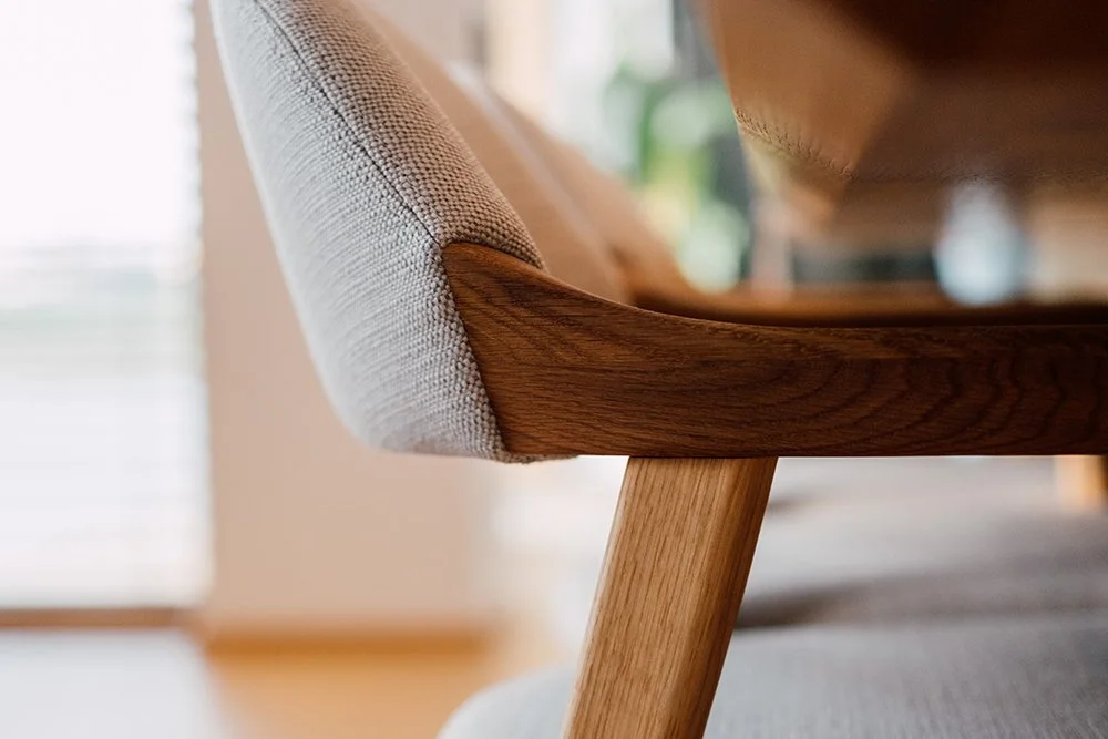 Nahaufnahme eines modernen Sofas mit Holzrahmen und Stoffpolstern, im Hintergrund ein Fenster mit Tageslicht.