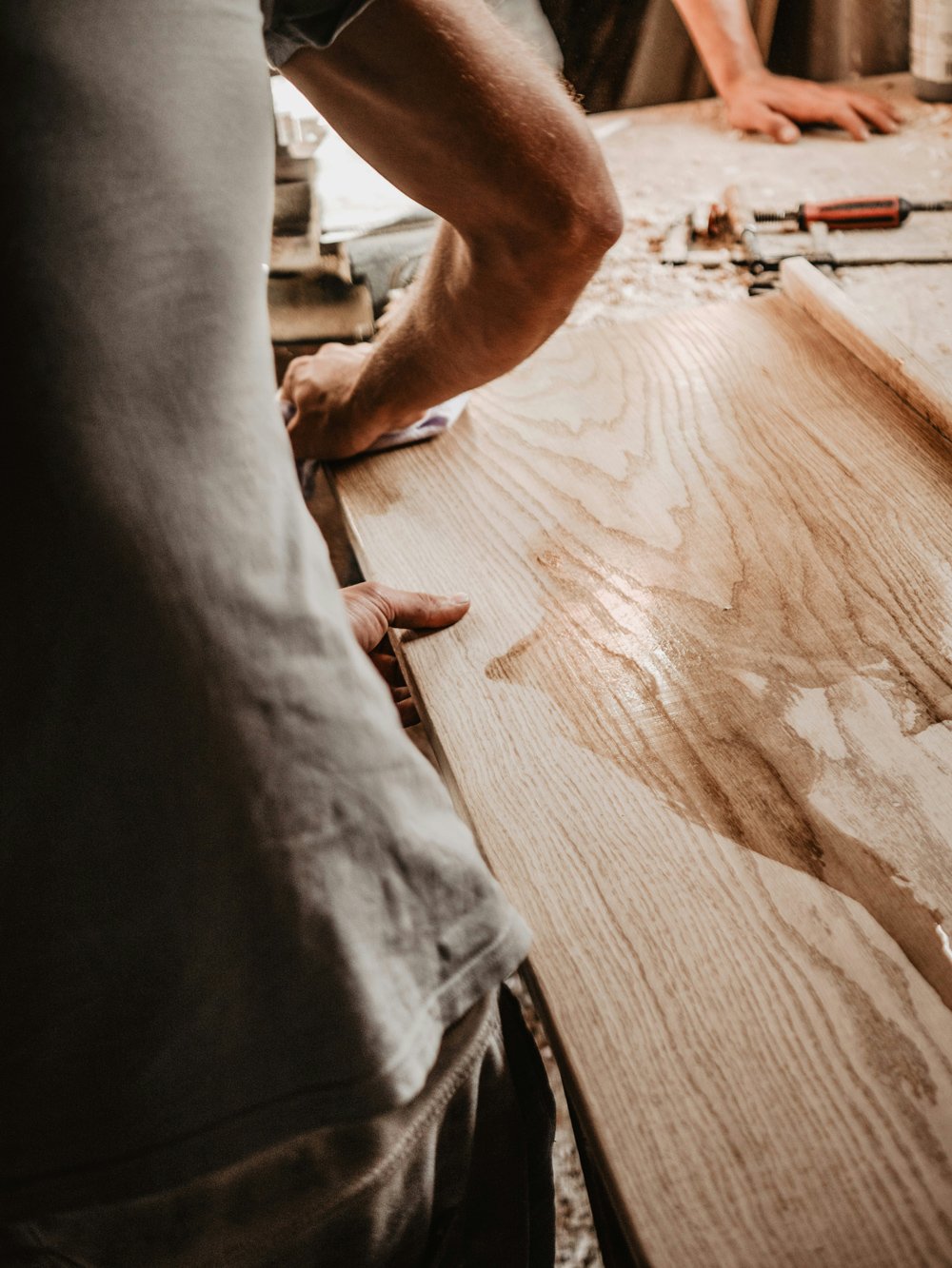 Ein Handwerker schleift eine große Holzplatte in einer Werkstatt.