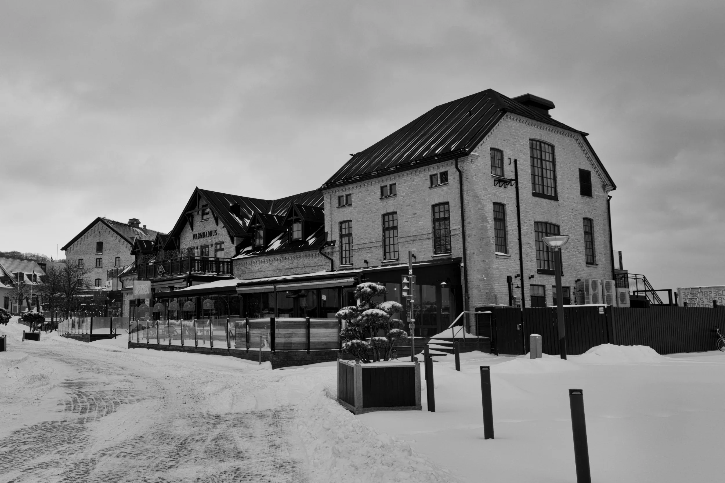 En svartvit bild av en vinterstad med snö på marken och Skansen hotell i Båstad i centrum, med flera stora fönster och en takås.