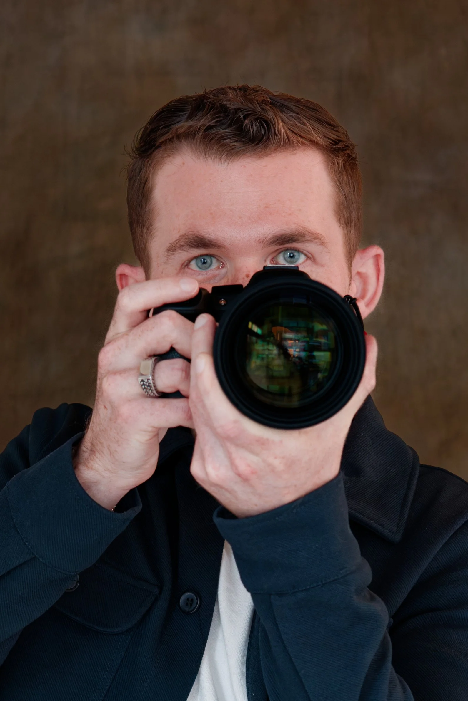 Man met blauwe ogen houdt een professionele camera recht voor zijn gezicht en neemt een foto, in een close-up portret.