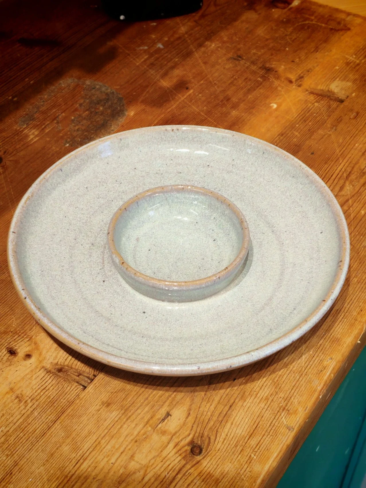 A ceramic dish with a small bowl in the center, placed on a wooden table.