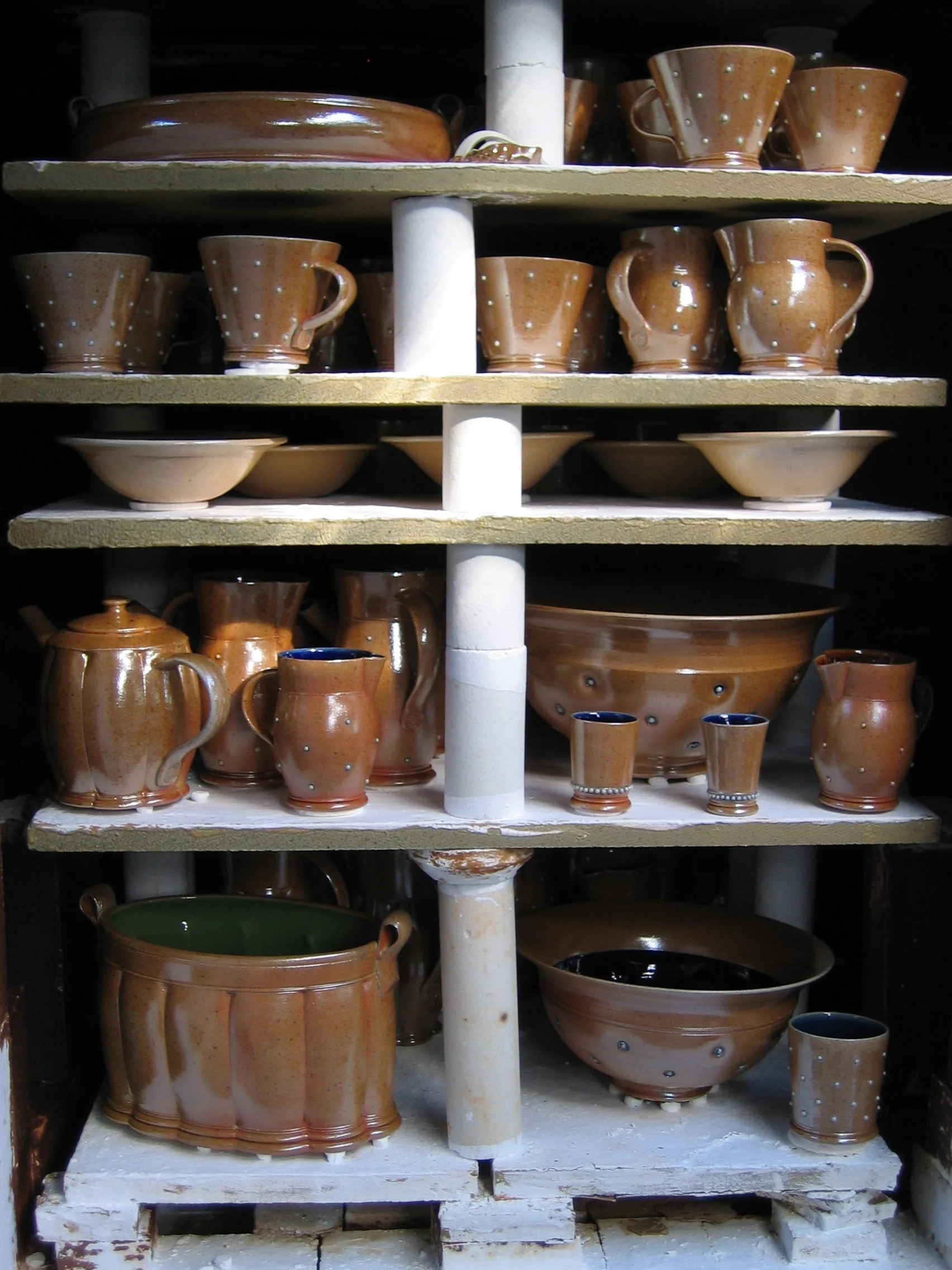 Shelves with various handmade brown pottery cups, bowls, and pitchers, some with white and blue decorative dots.