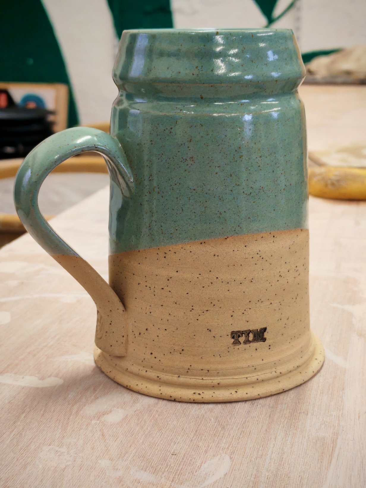 A ceramic mug with a beige bottom and a greenish top, featuring a handle on the left side and the word 'TIME' embossed near the bottom.
