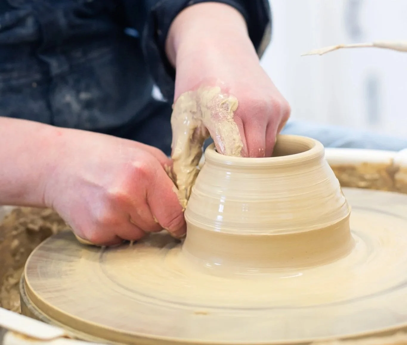 Person shaping a clay pot on a potter's wheel.