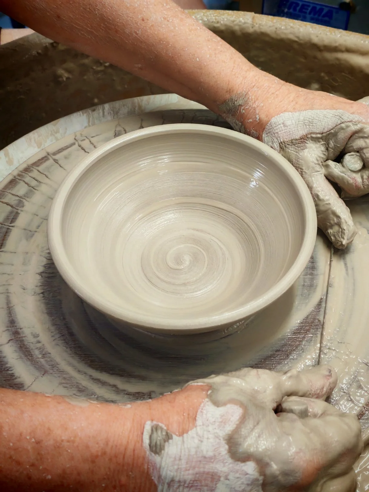 Person shaping a ceramic bowl on a pottery wheel in a workshop.