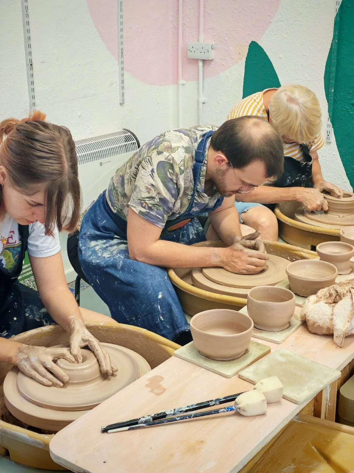 People participating in a pottery class, shaping clay on pottery wheels.