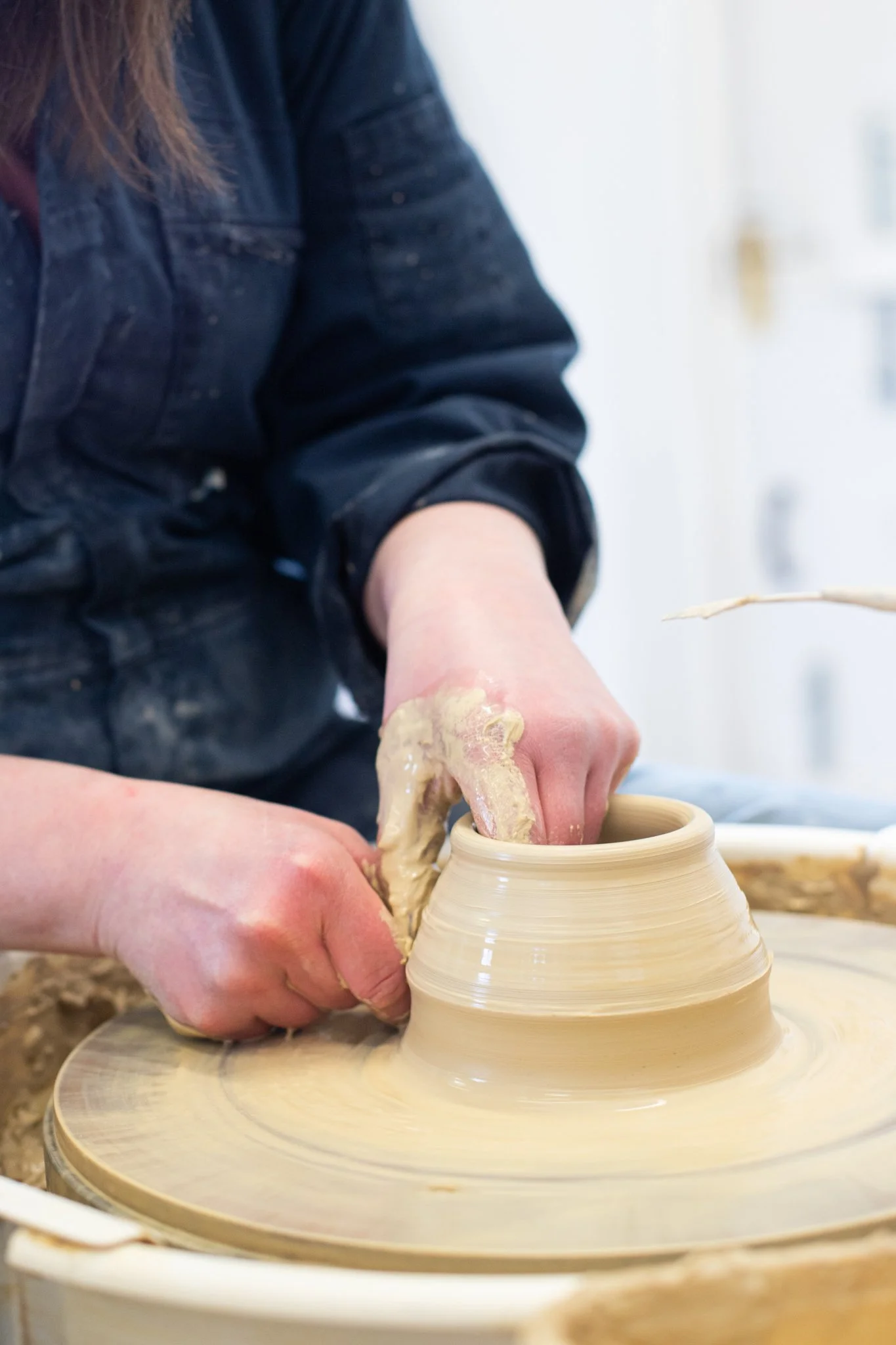 A person shaping a clay vase on a pottery wheel.