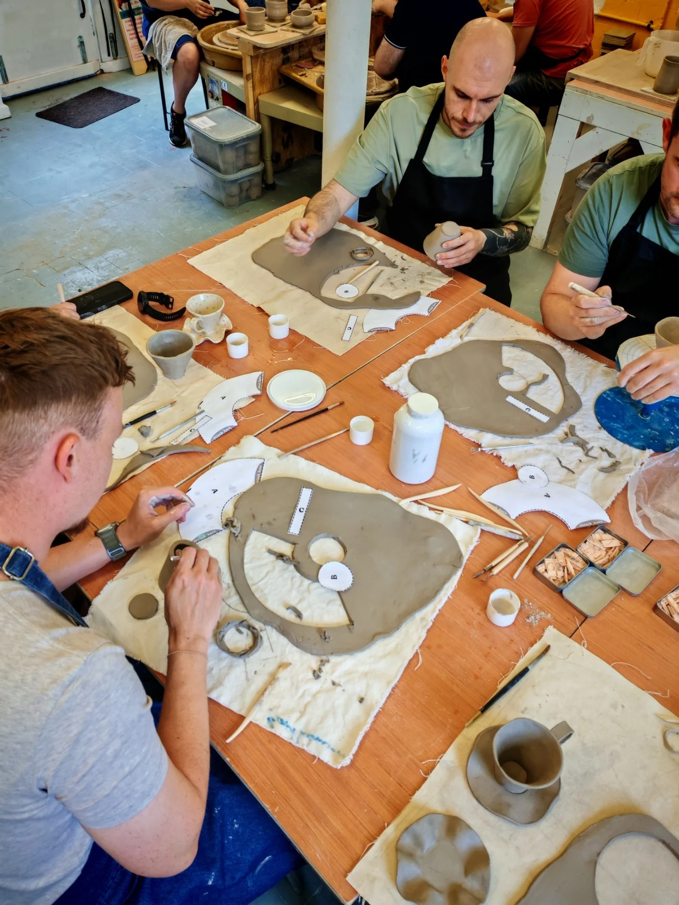 Group of people making pottery on a wooden table with clay, tools, and ceramic pieces.