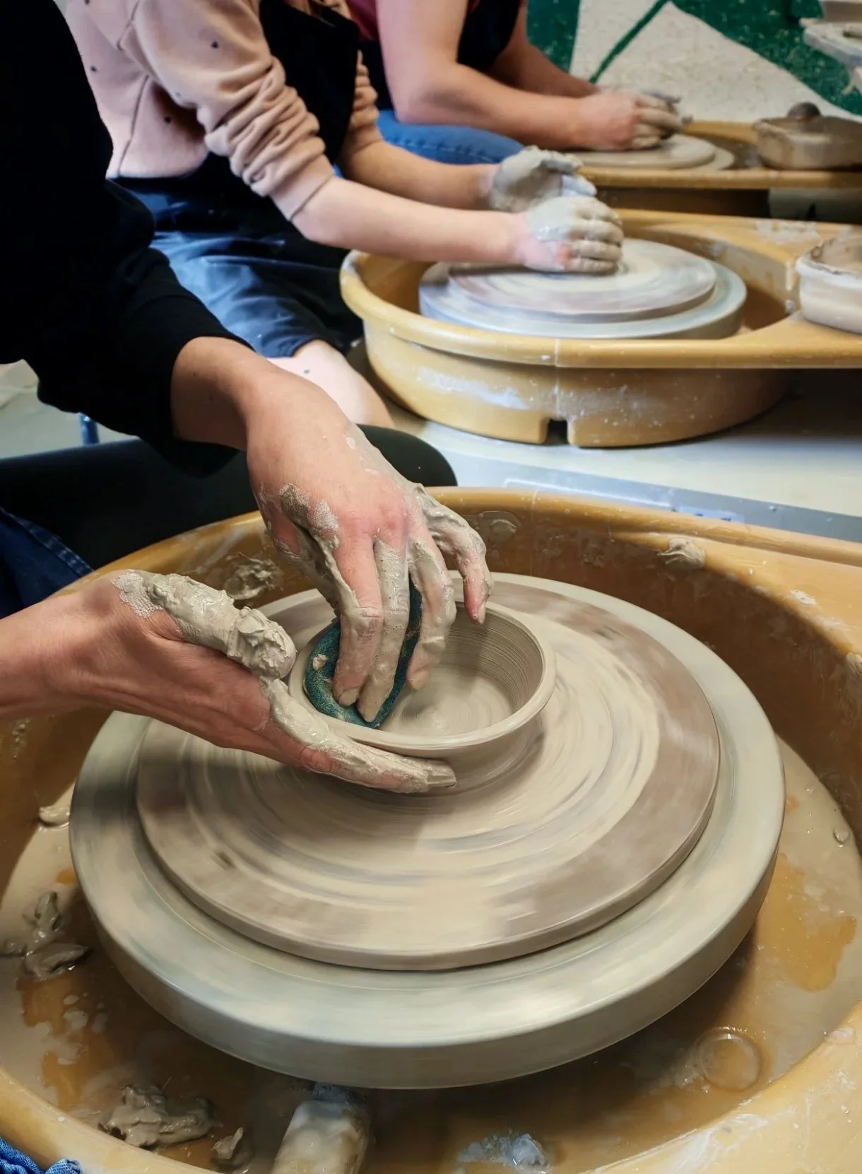 People creating pottery on a pottery wheel in a ceramic studio.