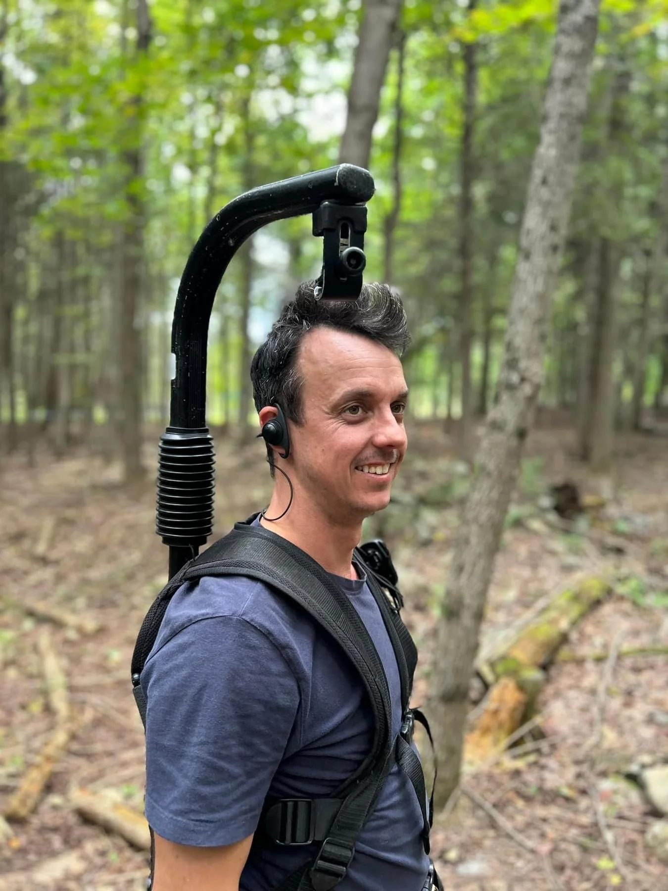 Un homme dans une forêt portant un équipement de marche avec un casque audio et un appareil photo suspendu au cou.