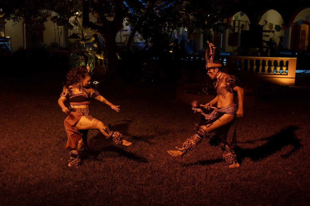 Two performers in traditional tribal costumes dancing outdoors at night.