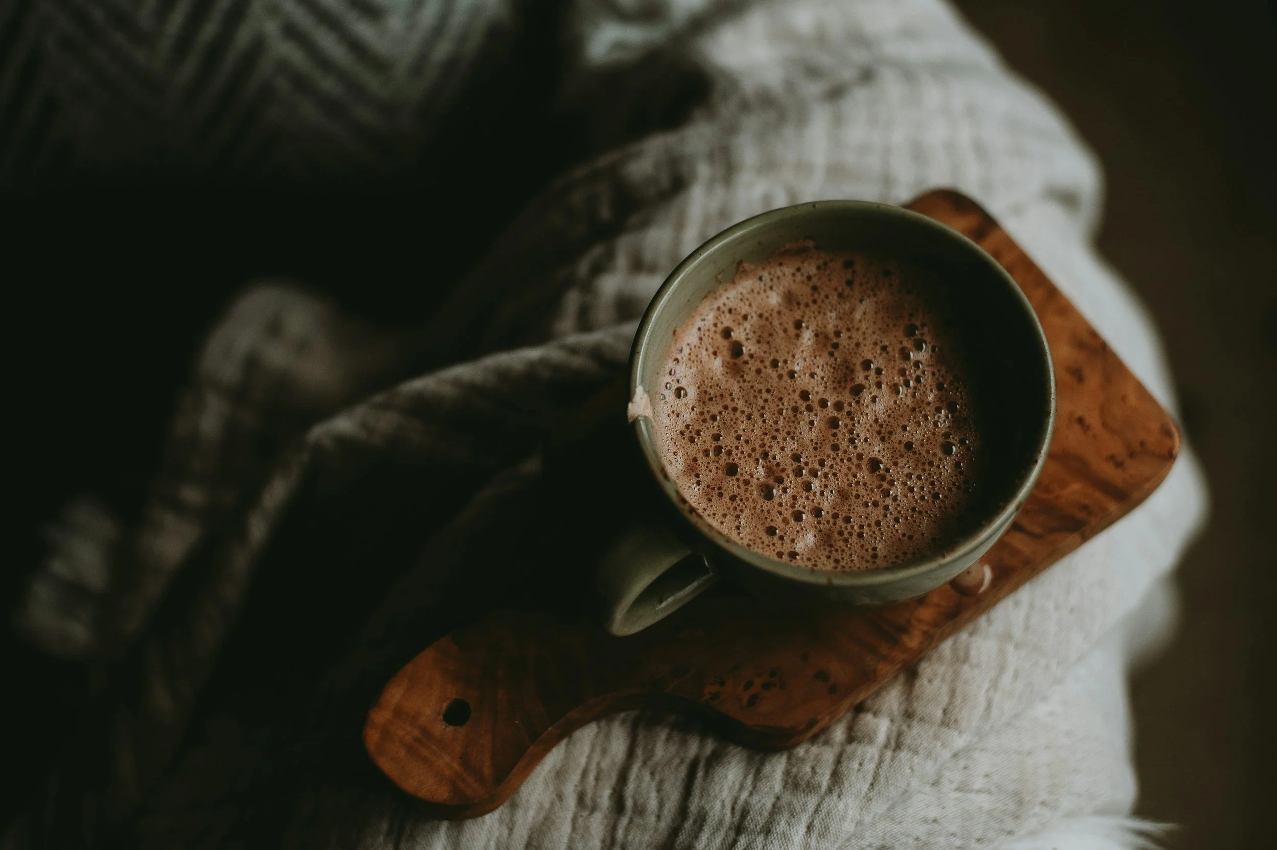 A mug of hot chocolate with foam, placed on a wooden tray.
