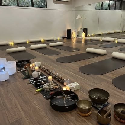 Yoga mats, bolsters, and candles arranged for a class in a peaceful studio with a variety of singing bowls and meditation tools at the front.