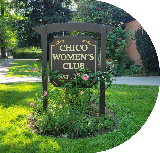 Sign for Chico Women's Club surrounded by pink roses and green bushes, with a sidewalk and trees in the background.