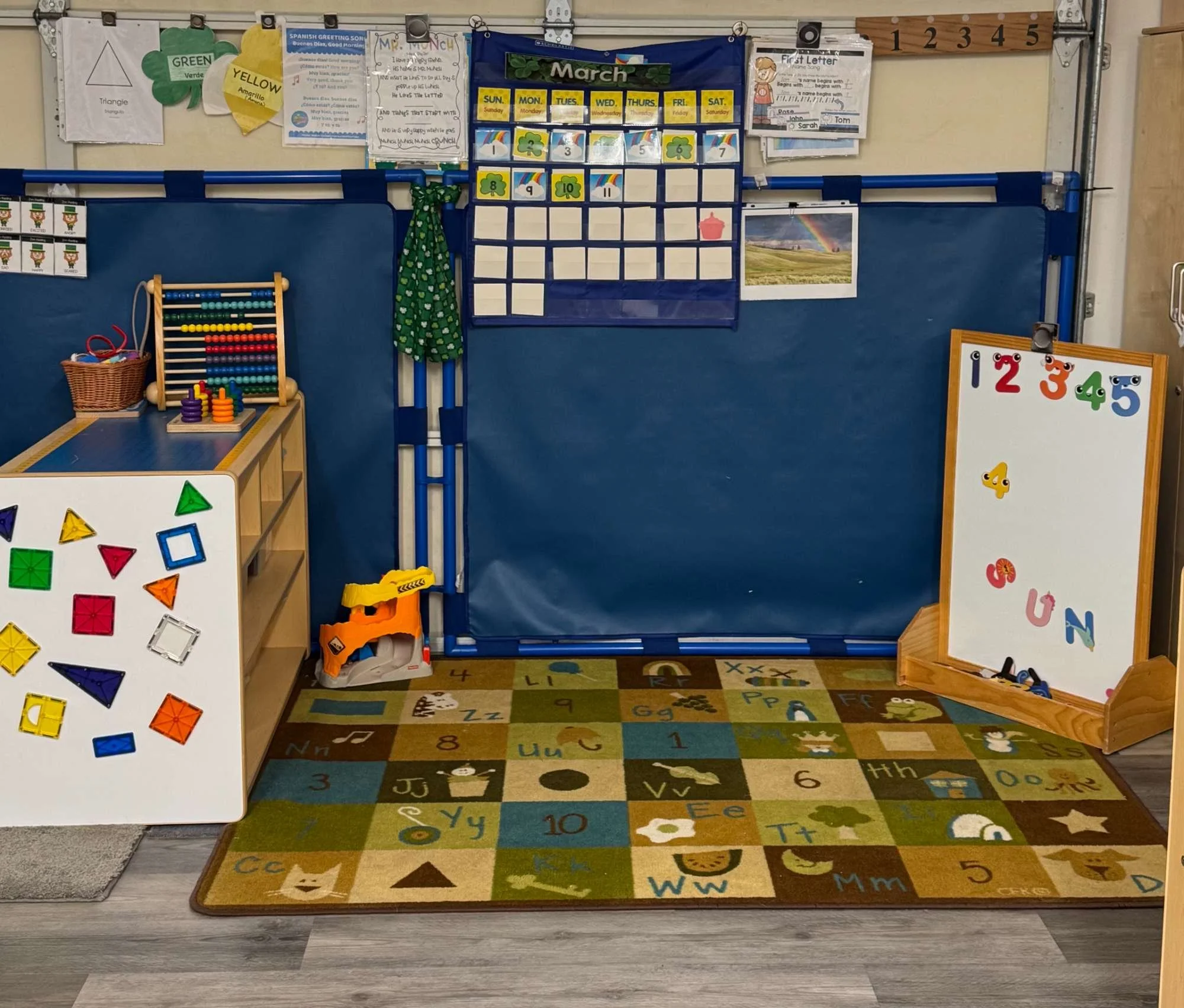 Classroom area with educational toys, whiteboards, and a colorful alphabet-themed rug.