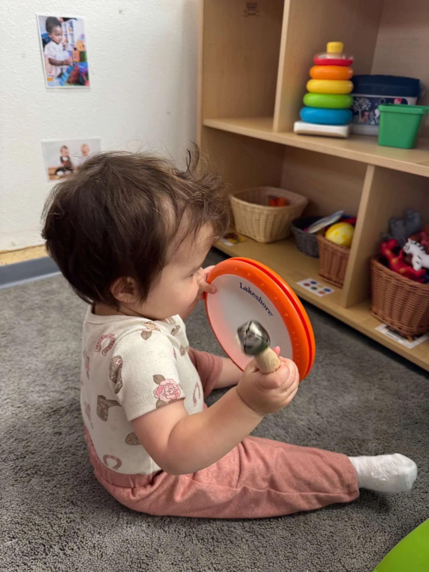 A young child with short dark hair sitting on a gray carpet, holding a round wooden toy.
