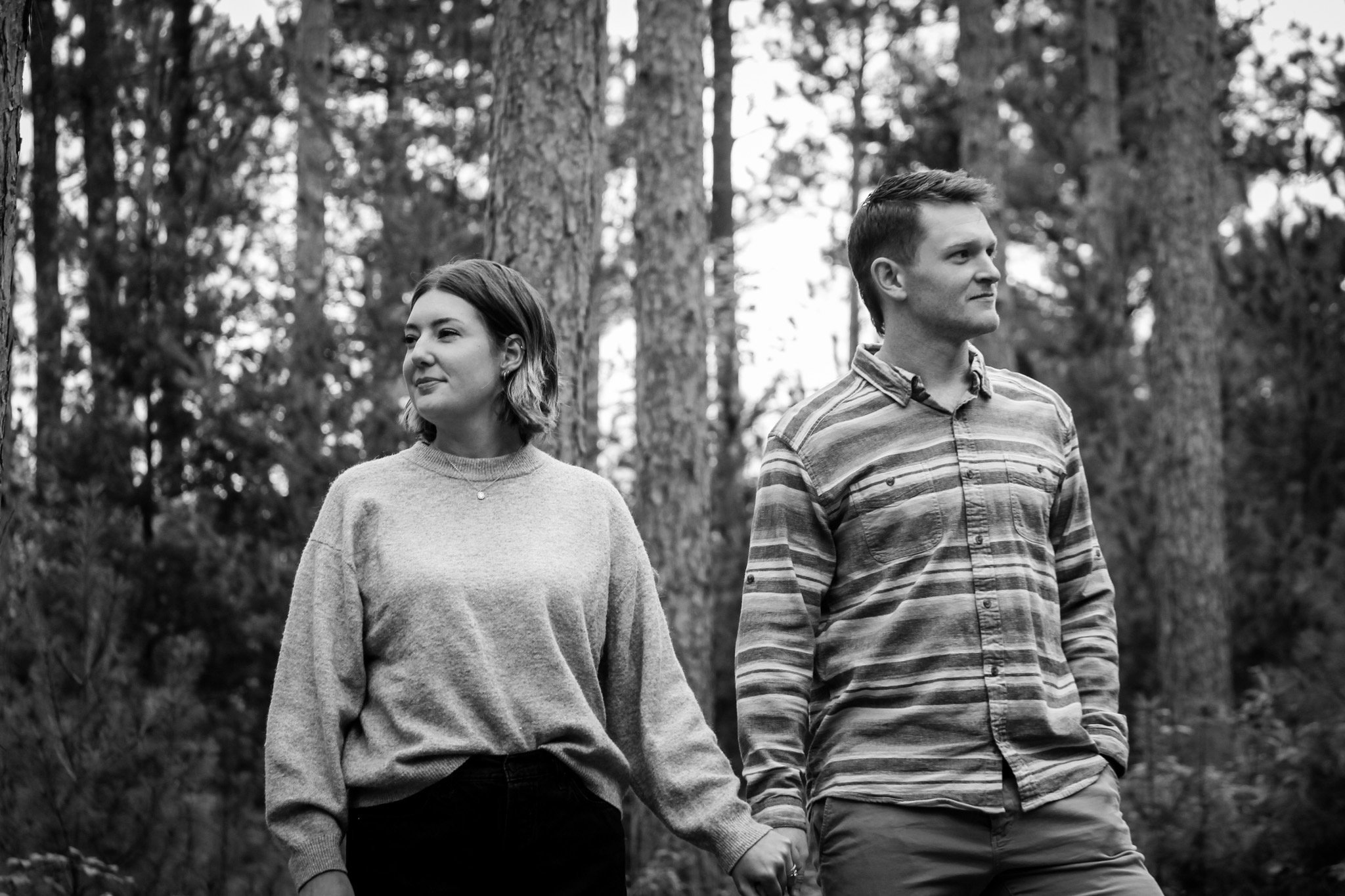 A young couple holding hands walking in a forest, black and white photo.