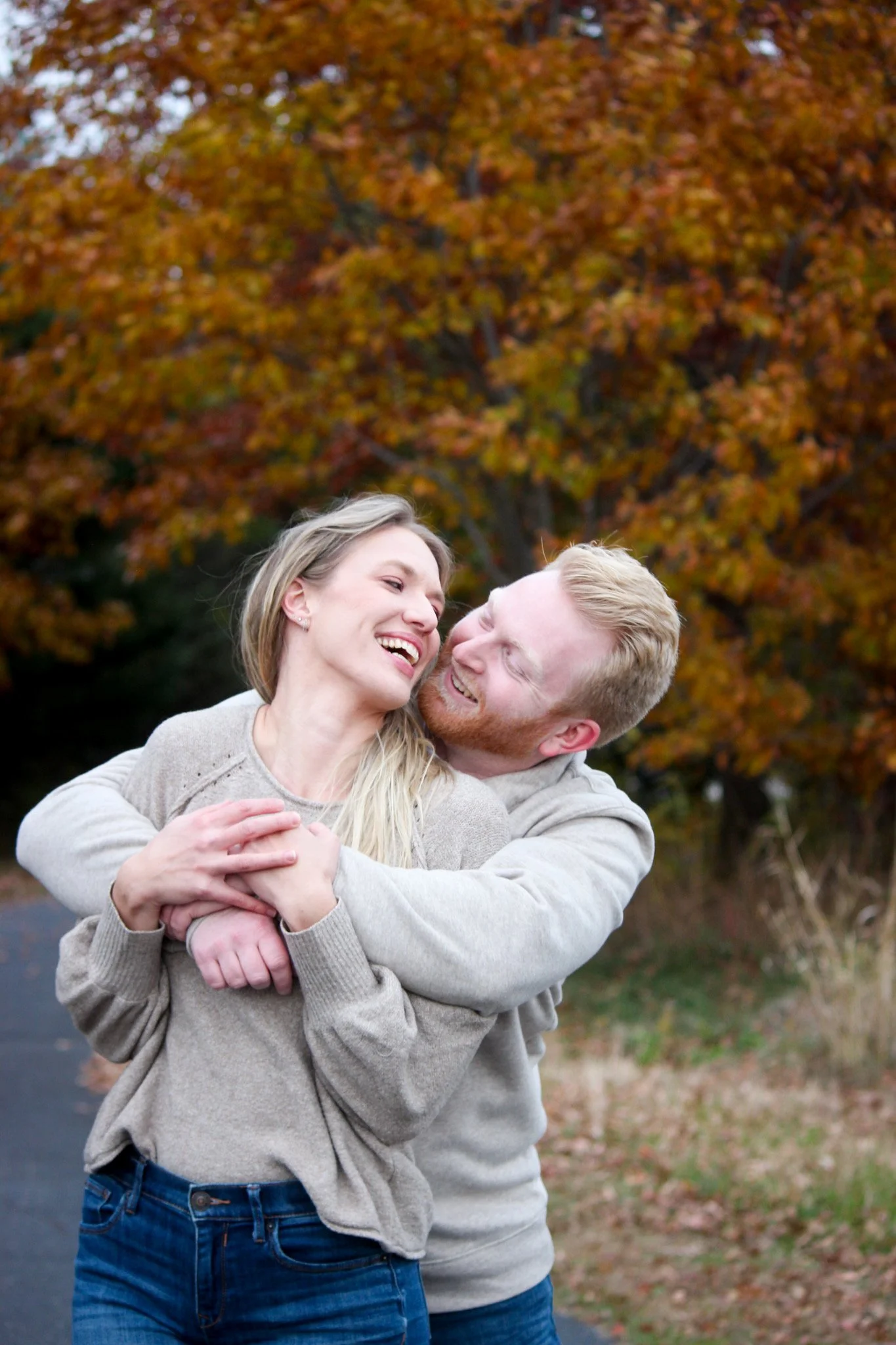 A young couple happily embracing outdoors during fall with orange autumn leaves in the background.