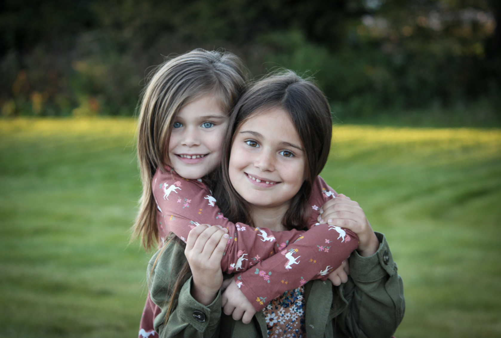 Two young girls hugging outdoors in a grassy park