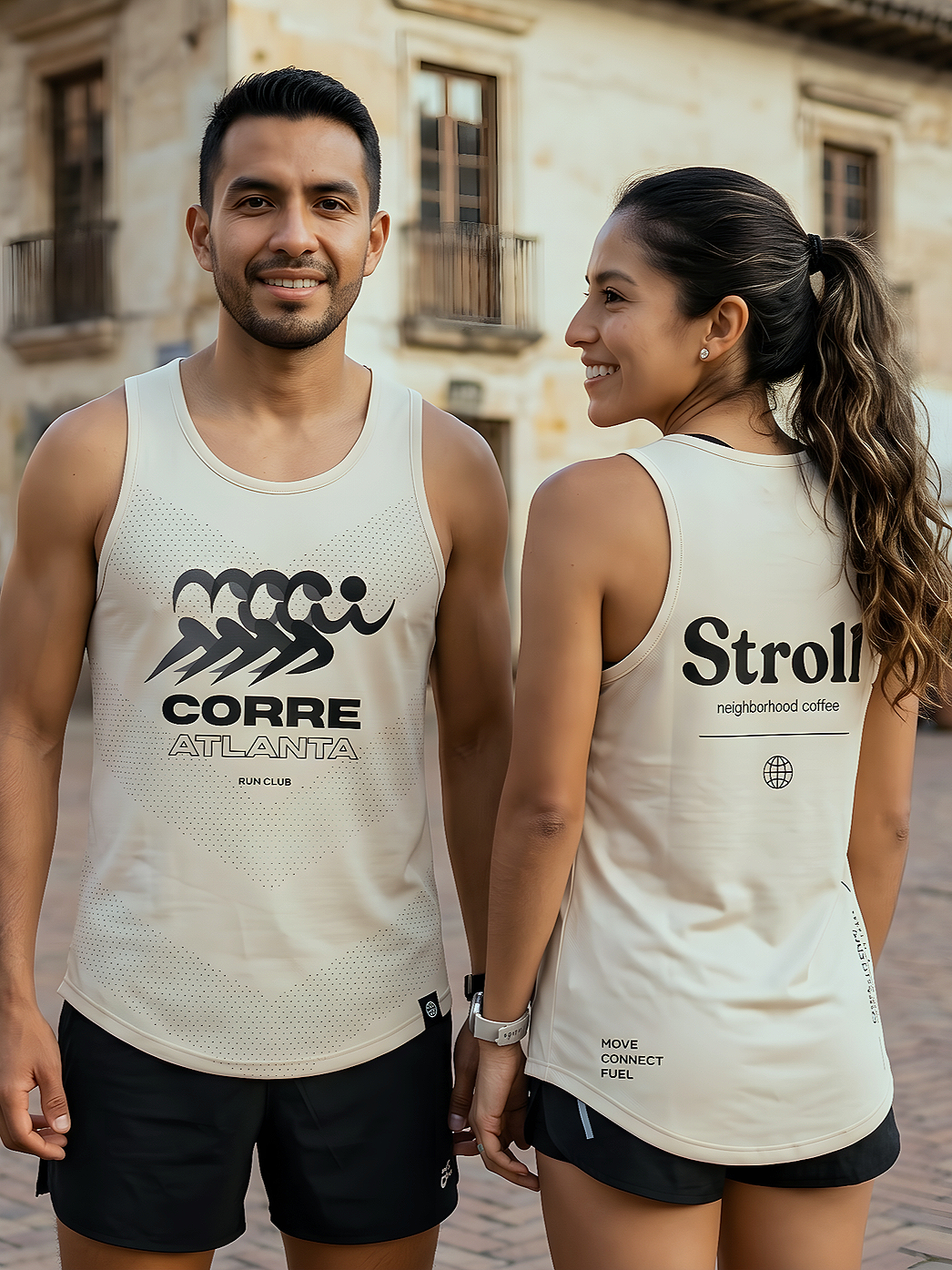A man and woman in athletic wear standing outside on a cobblestone street, holding hands, smiling, with old buildings in the background.