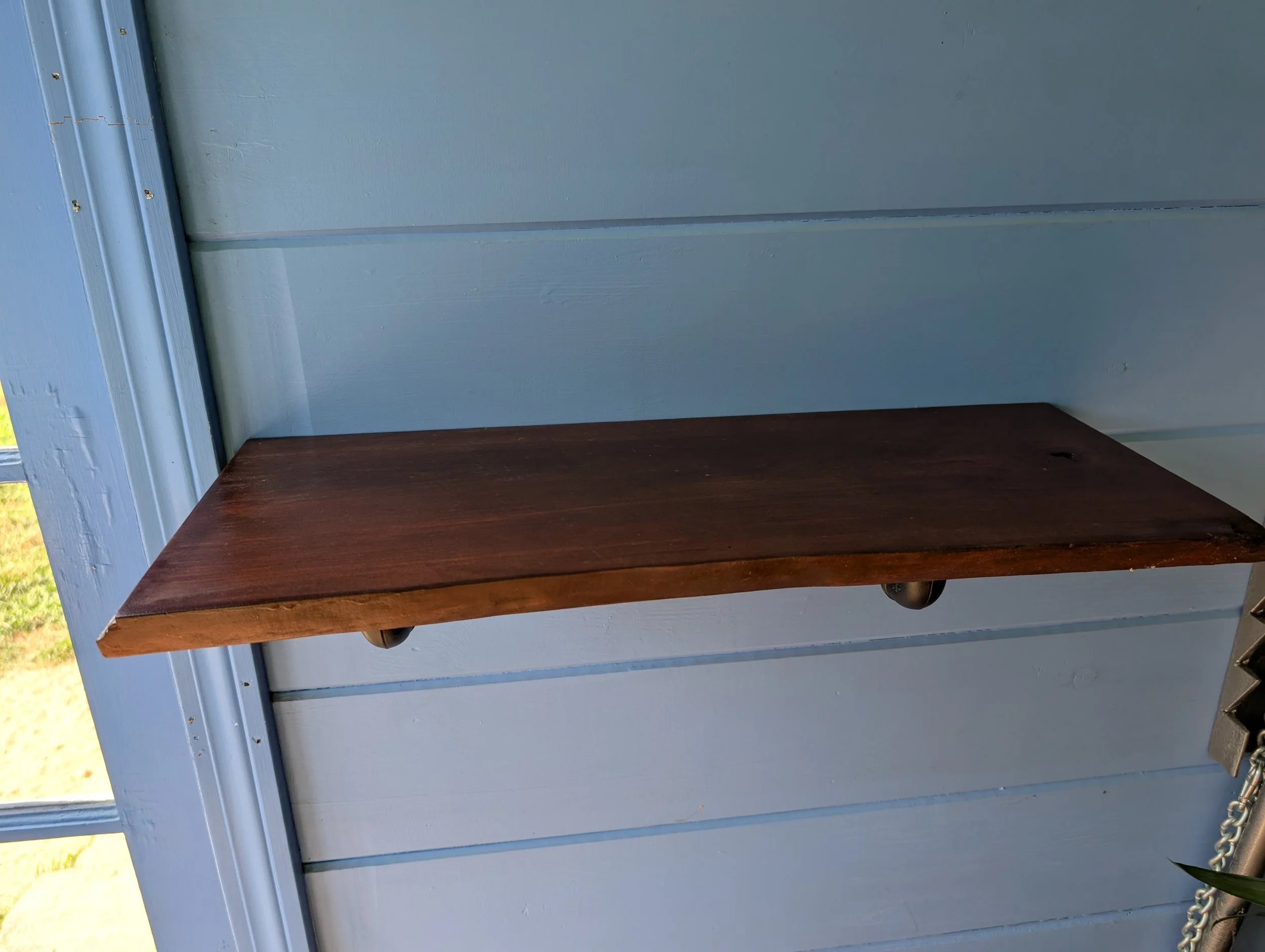 A wooden shelf mounted on a blue painted wall outside a house.