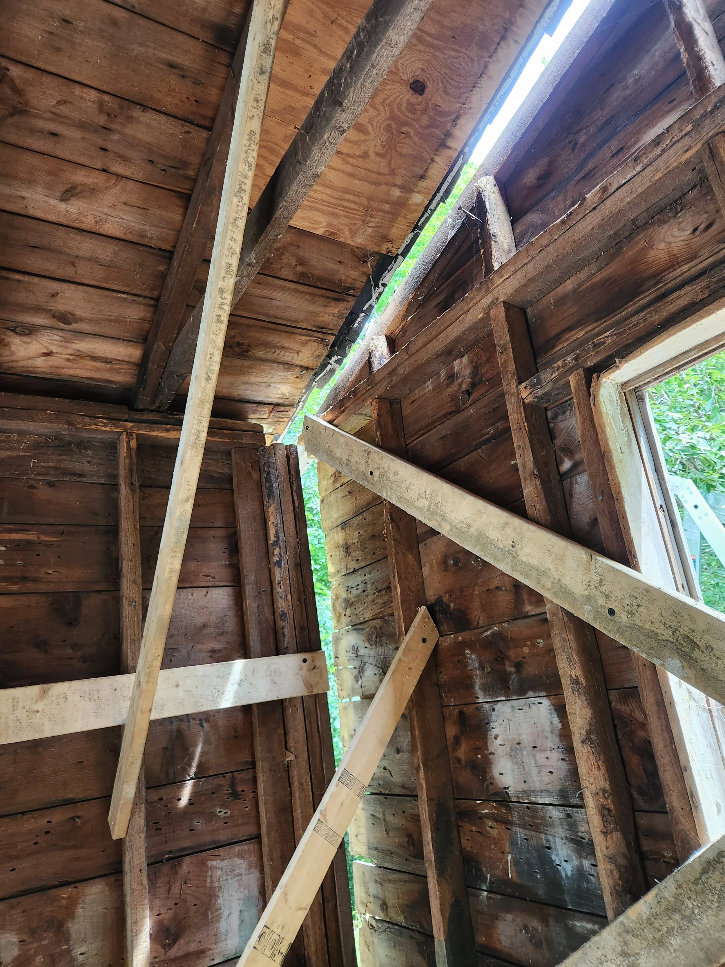 Interior of a wooden structure under construction with exposed beams and walls, and an open window.