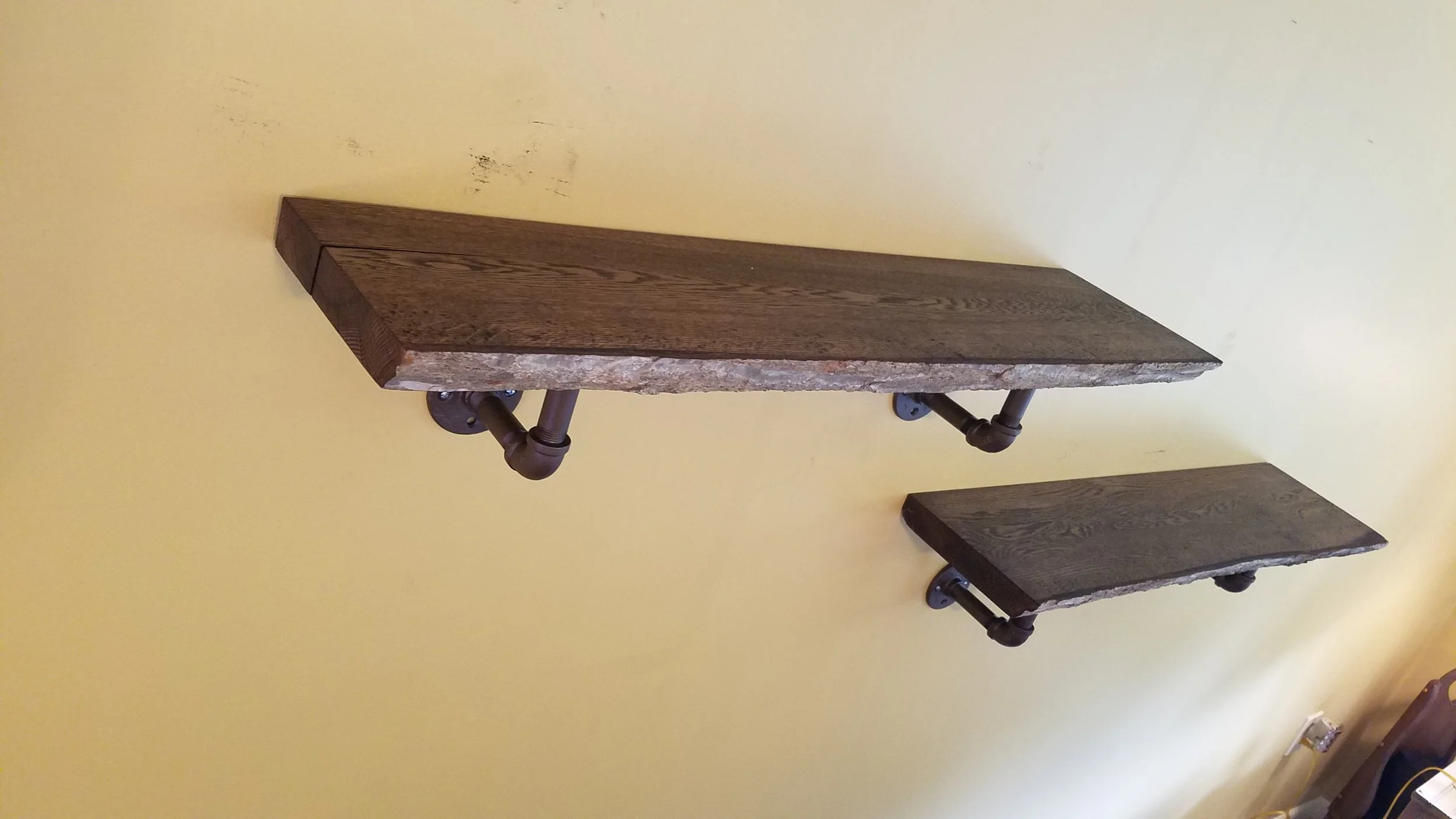 Two wooden shelves supported by metal piping brackets mounted on a yellow wall.