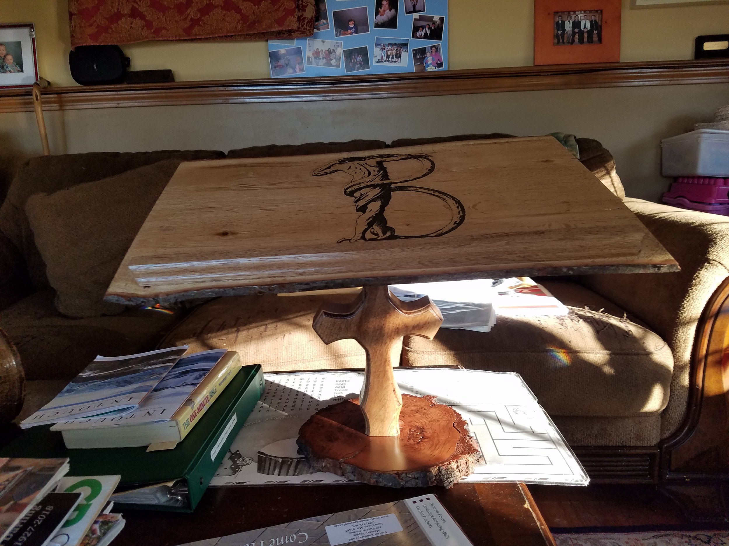 A wooden table with an engraved eagle design on the top, set on a carved wooden base, placed on a pile of books and papers in a cozy living room.