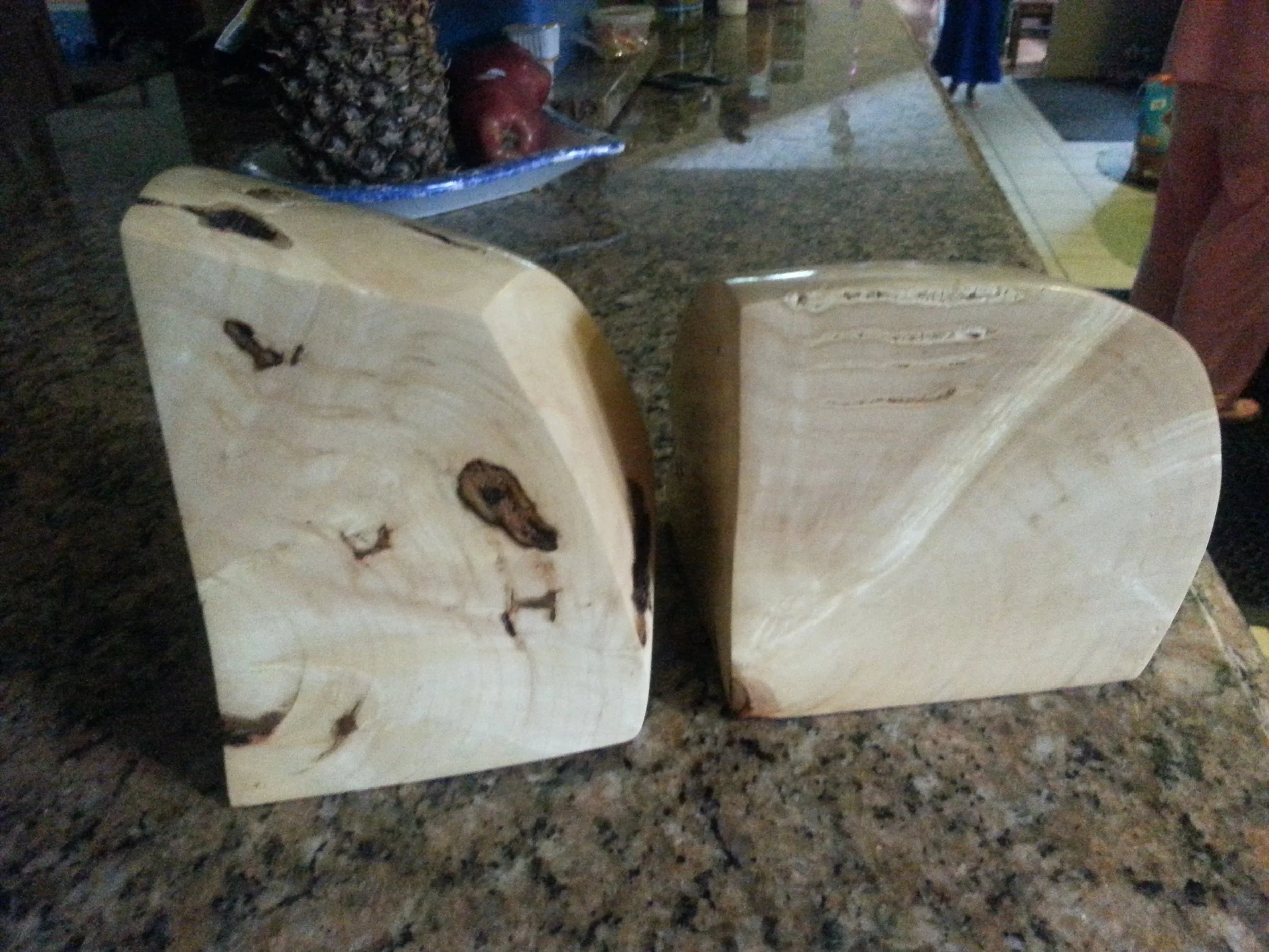 Two wooden blocks with natural wood grain and knots are placed on a countertop, with a bakery or market in the background.