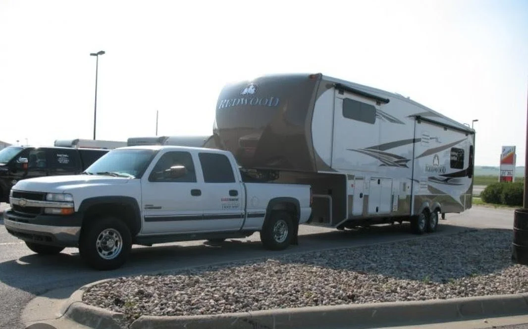 Silver pickup truck towing a large recreational vehicle (RV) trailer parked in a lot.